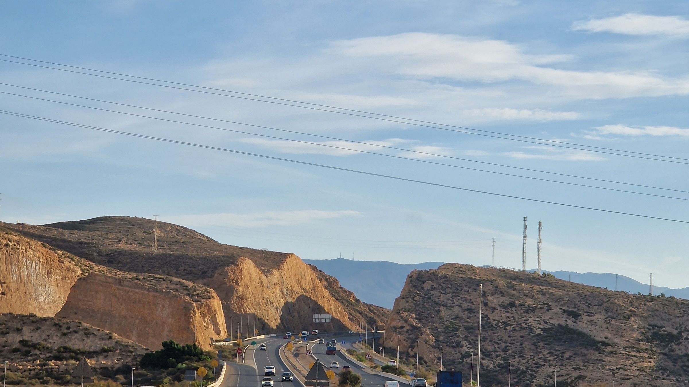 Motorway running through dry Mediterranean hills under a wide blue sky