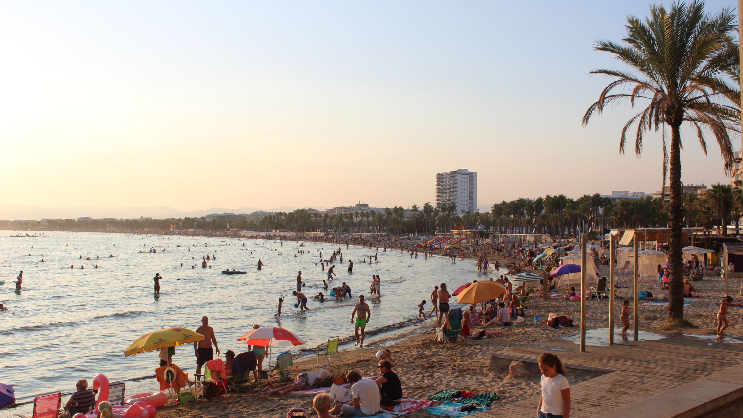 Long curving sandy beach at Salou with shallow calm water and a palm-lined promenade behind