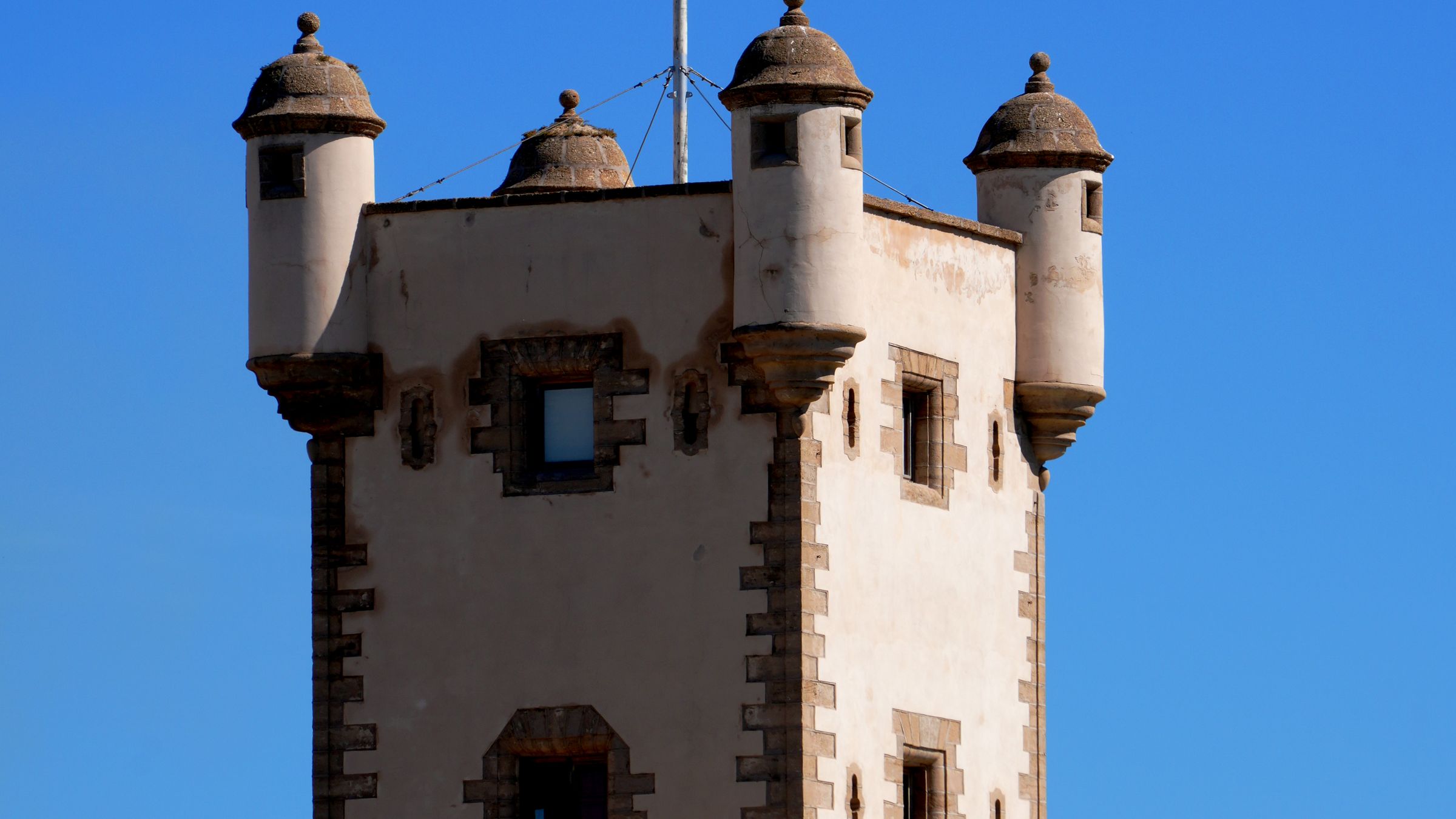 Square coastal watchtower with corner sentry turrets on a battlemented sea wall
